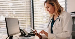 Locum tenens physician using a tablet while sitting at a desk in a doctor's office