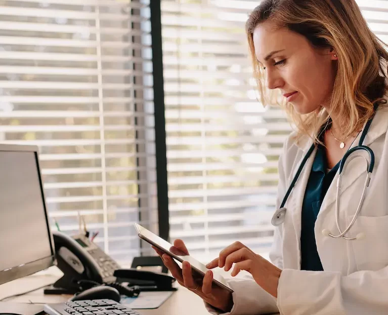 Locum tenens physician using a tablet while sitting at a desk in a doctor's office