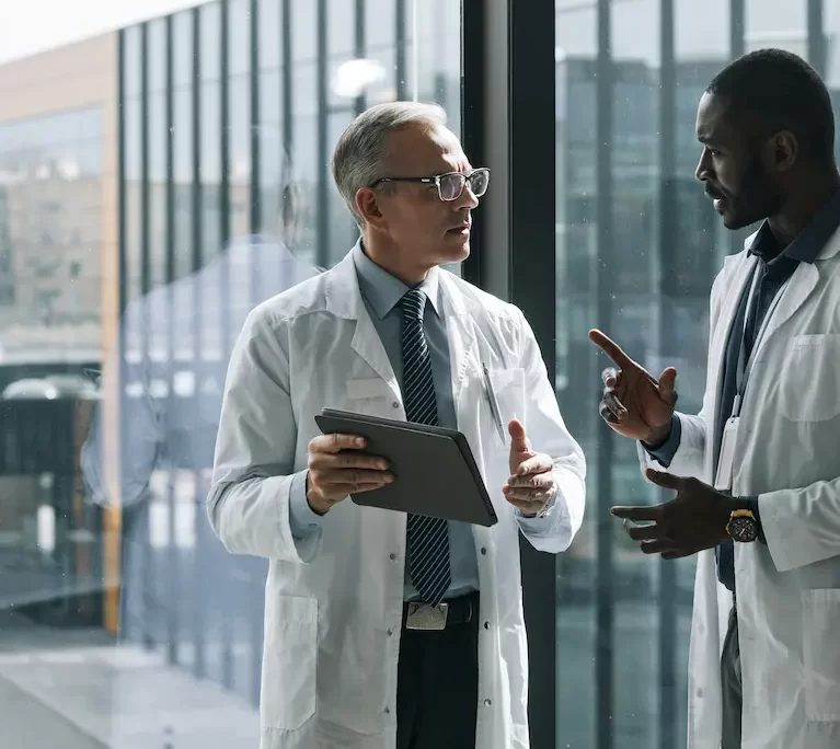 Two locum tenens physicians talking in front of a window while holding a tablet