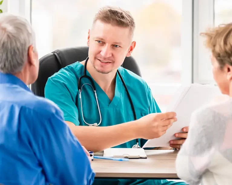 Locum internist speaking with an elderly couple while sitting at a desk.